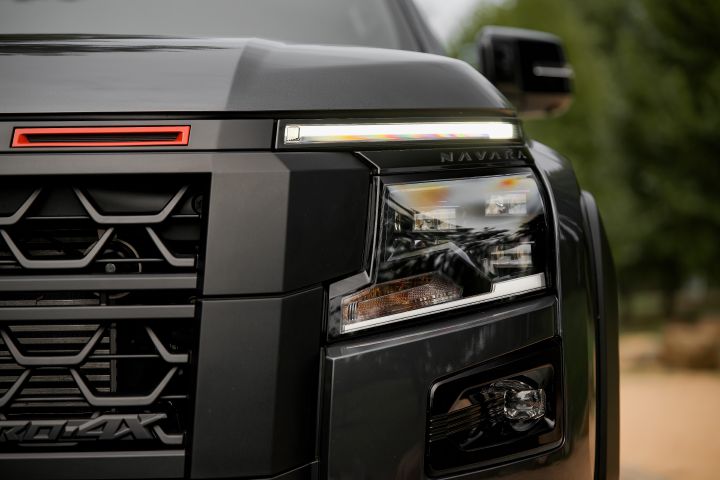 2026 Nissan Navara PRO-4X finished in Boulder Grey showing the front corner with headlight cluster, upper LED light, grille edge and black bumper trim.