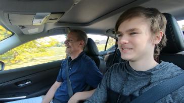 Teenage boy and an older man driving in a Nissan Vehicle.