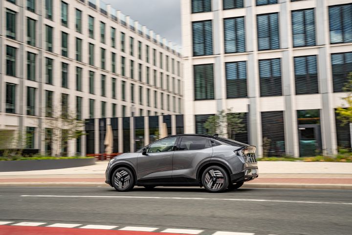 Blick auf Seite und Heck eines grauen Nissan Leaf, der an Hochhäusern vorbei über eine Stadtstraße fährt