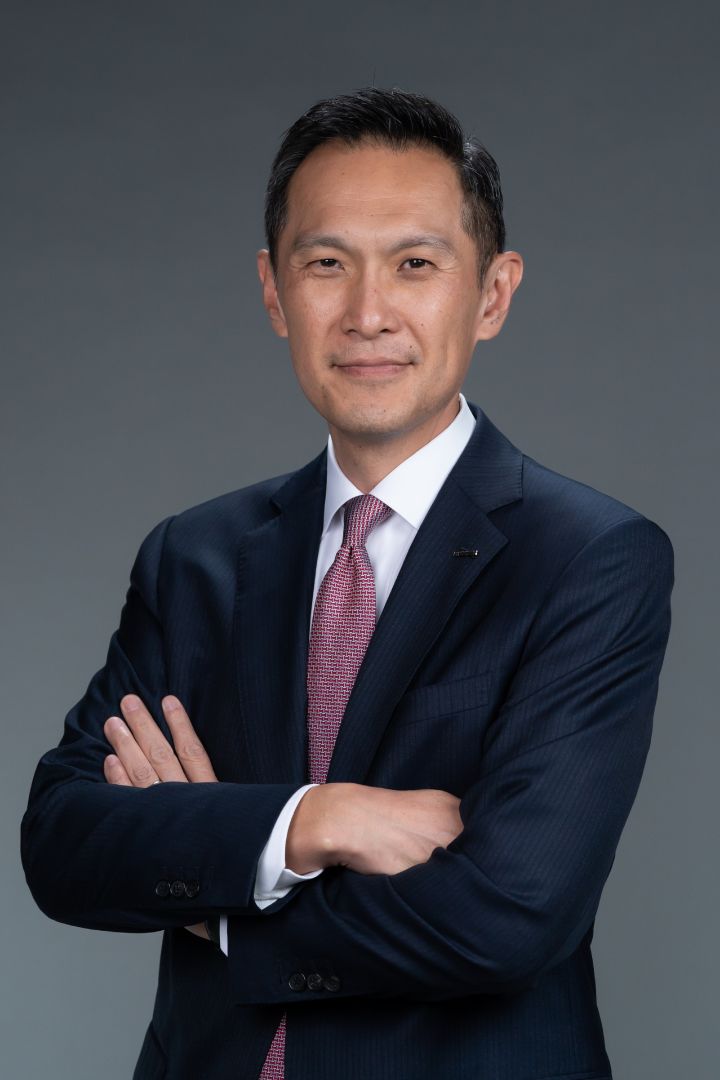 Portrait of Stephen Ma with his arms folded (suit, tie and NISSAN corporate pin)