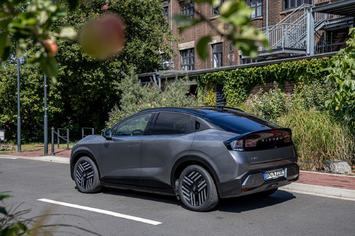 3/4 Heckansicht eines parkenden grauen Nissan Leaf, oben ragt ein Zweig mit einem Apfel ins Bild.
