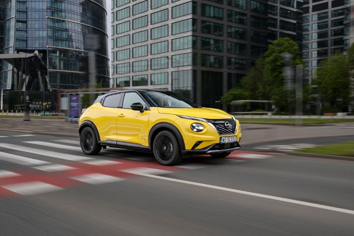 Jadący żółty Nissan Juke (widok z półprofilu) z budynkami w tle