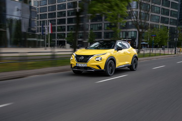 Jadący żółty Nissan Juke (widok z półprofilu) z budynkami w tle
