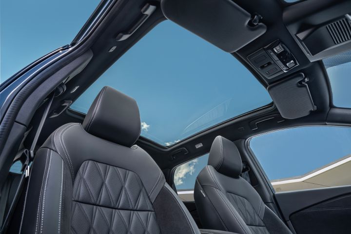 Blick vom Beifahrersitz durch das großzügige Panorama-Glasdach des Nissan Qashqai auf einen blauen Himmel