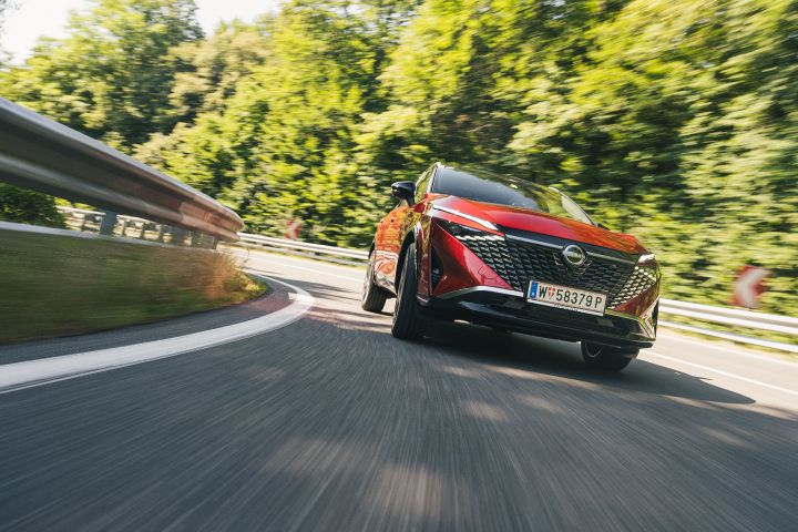 Frontaler Blick von unten auf einen Nissan Qashqai in Fuji Sunset Red, der schnell durch eine Kurve fährt