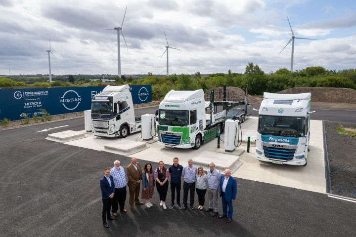 In einem Halbkreis stehen zehn Personen nebeneinander vor drei elektrischen Lkw an Ladesäulen, im Hintergrund ist das Nissan Logo zu sehen.