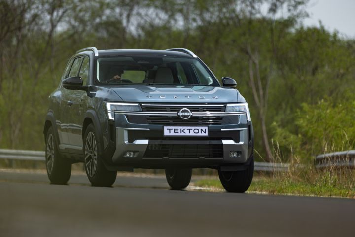 Low-angle front view of the Nissan Tekton driving on a tree-lined road.