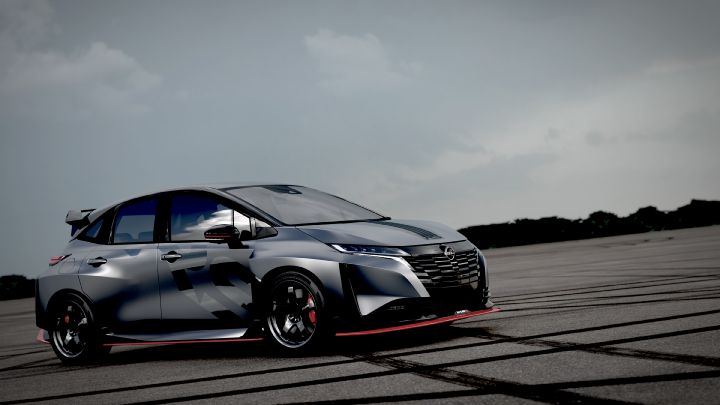A silver and black two-tone sports car, the Aura Nismo RS Concept, parked on an outdoor skid pad in a left-side angled view. The vehicle features a low stance and a large rear wing, with black wheels and visible red brake calipers. The side displays a light gray 'RS,' and a red accent line runs along the lower body. The background shows a cloudy sky and distant trees, with tire marks visible on the asphalt surface