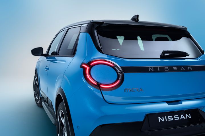 rear 5/8 side view of new Micra in gear blue color, lit headlamps, Micra / Nissan name plates, side doors and gelato scoop from rear to front
