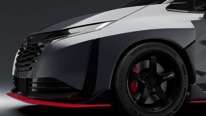 A close-up studio shot of the front-right section of the Aura Nismo RS Concept, a silver and black two-tone sports car. The image highlights the sharp LED headlight and black front grille, with a red accent line visible along the lower edge. The black wheel features a red brake caliper and the 'NISMO' logo. The background is dark gray, emphasizing the car's glossy finish and sporty details