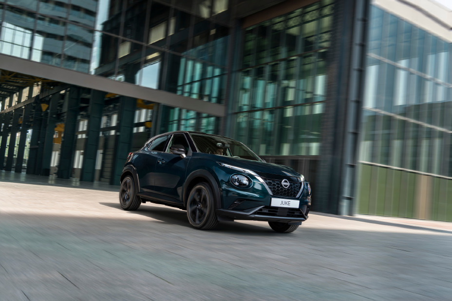 Le Nissan JUKE Pulse évoluant dans un environnement urbain moderne, capturé en mouvement avec une élégante carrosserie Ocean Deep se détachant sur des bâtiments aux façades vitrées.