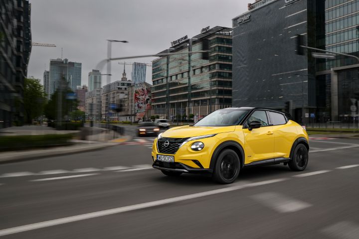 Jadący żółty Nissan Juke (widok z boku) z budynkami w tle