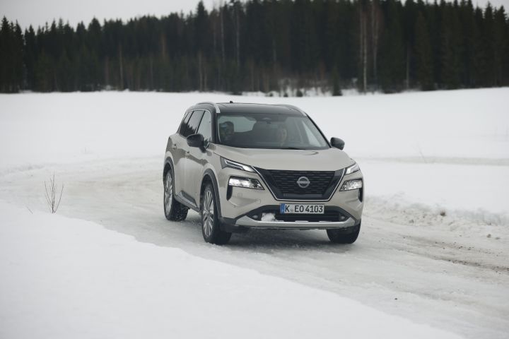 Silberner Nissan X‑Trail e‑Power e‑4ORCE kommt in verschneiter Landschaft aus einer verschneiten Kurve herausgefahren