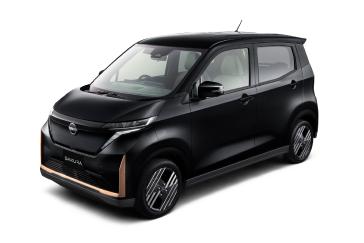 黒い「日産サクラ」を、無地の白背景の前で車両の左前方から斜めに撮影した画像。フロントマスクと側面が引き締まった印象で、車両全体が中央に配置されている。