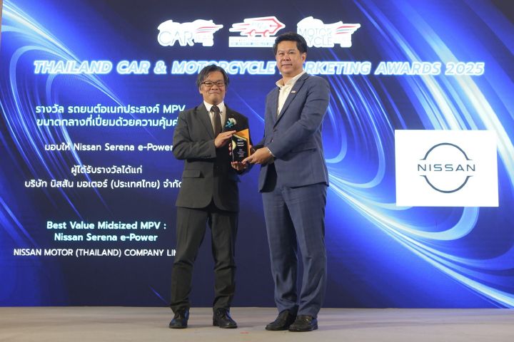 This image captures a moment from the Thailand Car & Motorcycle Awards 2022 ceremony. Two individuals are standing on stage—one presenting an award to the other—highlighting a formal and celebratory atmosphere. Behind them, a large digital screen displays the event title along with award details and the Nissan logo, indicating the brand's recognition at the event.