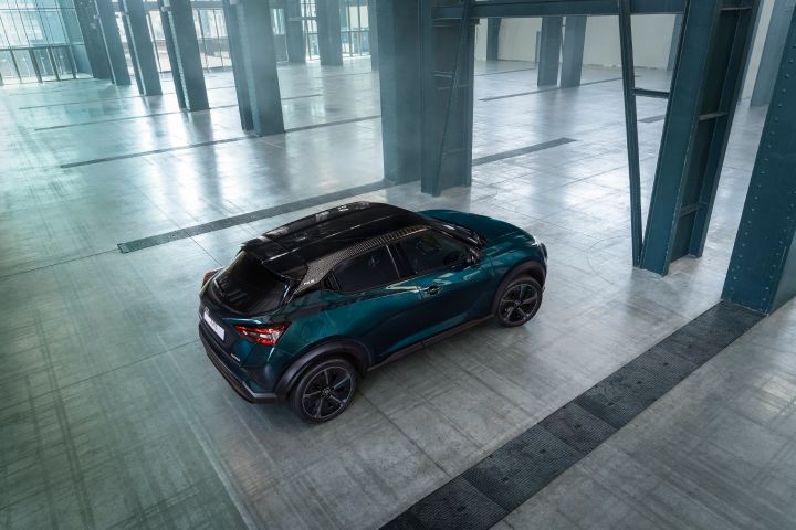 Top three-quarter rear view of the Nissan JUKE Pulse inside a large industrial space, highlighting the contrasting roof, rear design, and compact crossover proportions