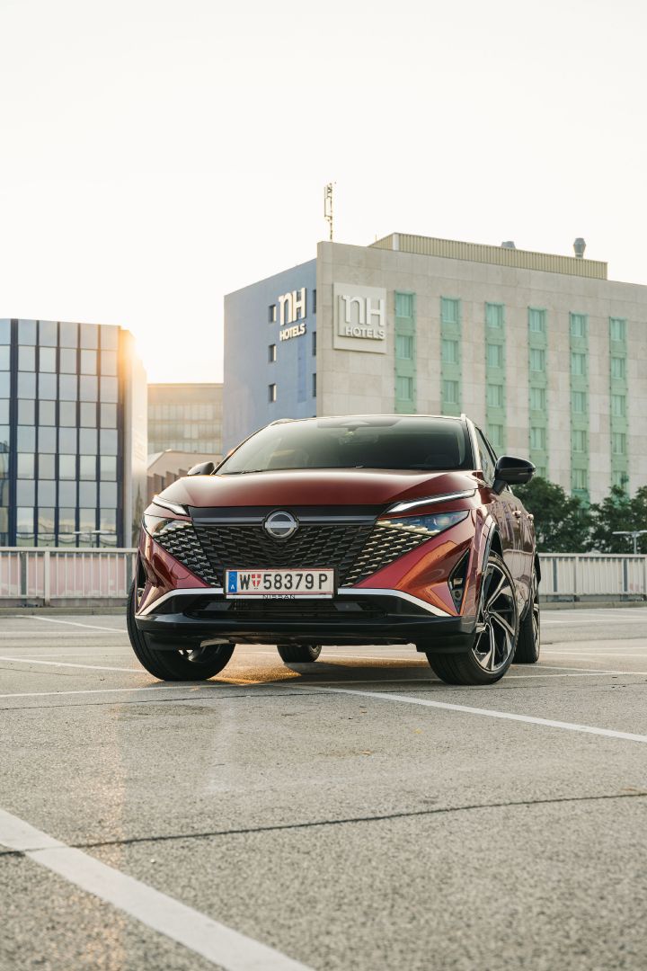 Frontansicht eines Nissan Qashqai in Fuji Sunset Red vor einem Hotelgebäude
