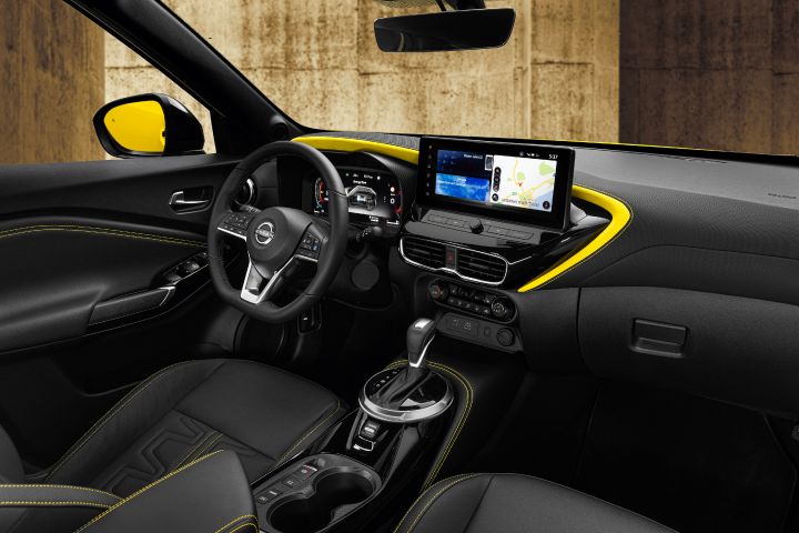 Het zwarte interieur van de Nissan Juke met in het midden een groot beeldscherm en een gele, boemerangvormige versiering