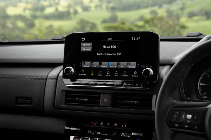 Front cabin view of a 2026 Nissan Navara ST-X showing the 9-inch Touch infotainment screen in the centre of the dashboard, tuned to Nova 100, with central air vents, physical shortcut buttons, and dual-zone climate controls below.