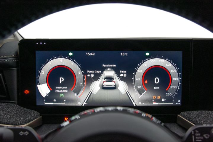 Painel digital de carro com velocímetro, conta-giros e imagem central mostrando um veículo com alertas de ponto cego, faixa e obstáculos à frente