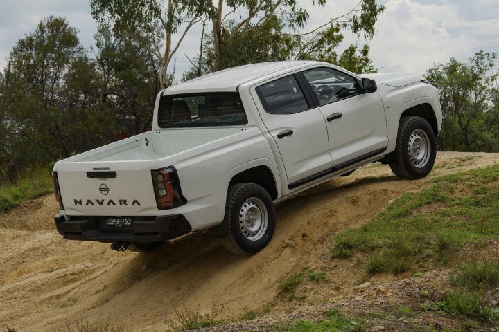 2026 Nissan Navara SL dual cab ute finished in Alpine White shown from the rear-left climbing a sandy embankment, with the empty tub, tailgate badging and steel wheels visible.