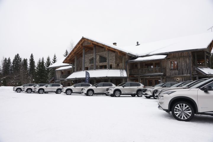 Zehn silberne Nissan X‑Trail e‑Power e‑4ORCE stehen im Schnee vor einem großen Holzhaus