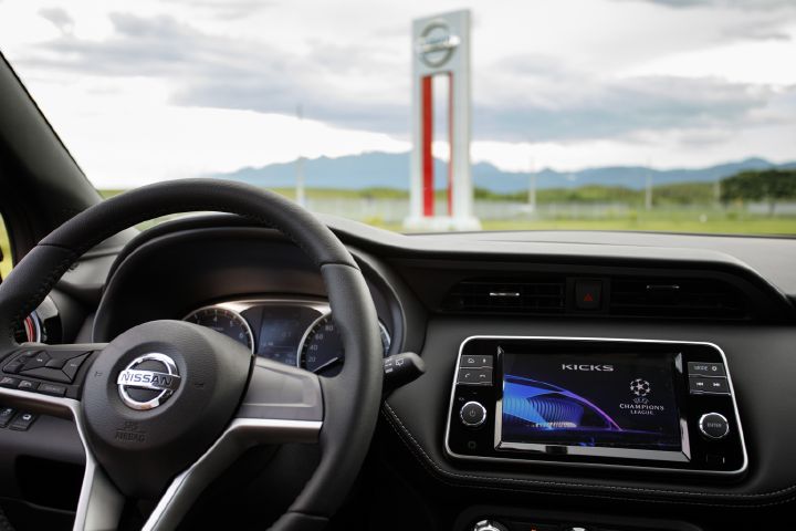 Detalhe do volante e do painel com o totem da fábrica da Nissan ao fundo
