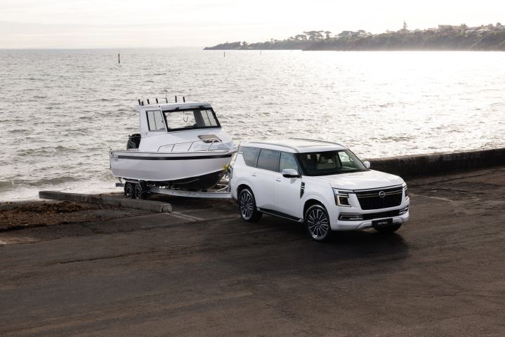 2026 Nissan Y63 Patrol finished in white, shown from a close front three-quarter exterior angle towing a large white boat on a trailer at a coastal boat ramp.