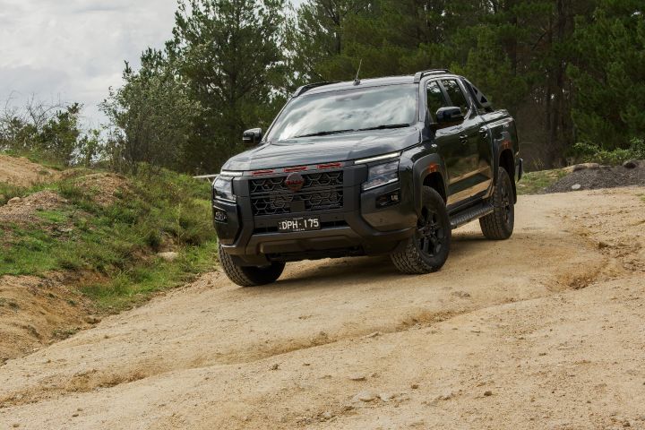 2026 Nissan Navara PRO-4X finished in Boulder Grey descending from the front three‑quarter with red grille slats, plate DPH‑175 and side step clearing the rut.