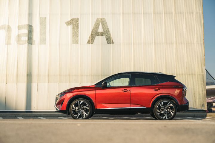 Ein Nissan Qashqai in Fuji Sunset Red steht seitlich vor einem fensterlosen Flughafengebäude