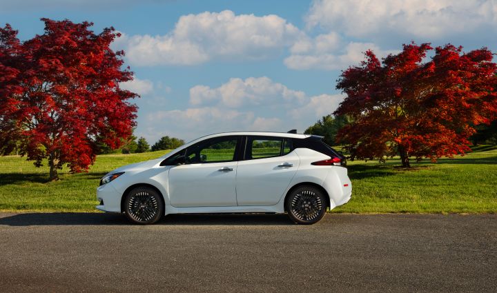 White Nissan LEAF with green grass, cloudy sky and red trees in background