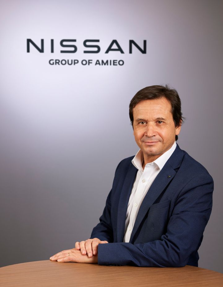 A photo of Jordi Vila smiling while sitting at table in front of Nissan logo