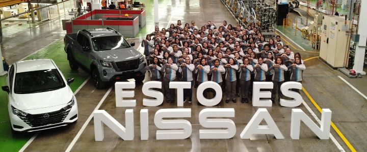 De fondo Planta CIVAC, Foto grupal con las mujeres de manufactura con uniforme y haciendo el símbolo de un corazón. Letrero al frente “Esto es Nissan” y por un costado una Nissan Frontier Gris y un Nissan Versa Blanco