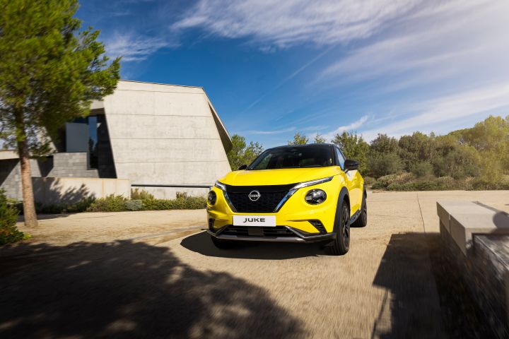 Fahraufnahme gelber Nissan Juke 3/4 Front auf hellem Untergrund vor hellem Gebäude und Wiese
