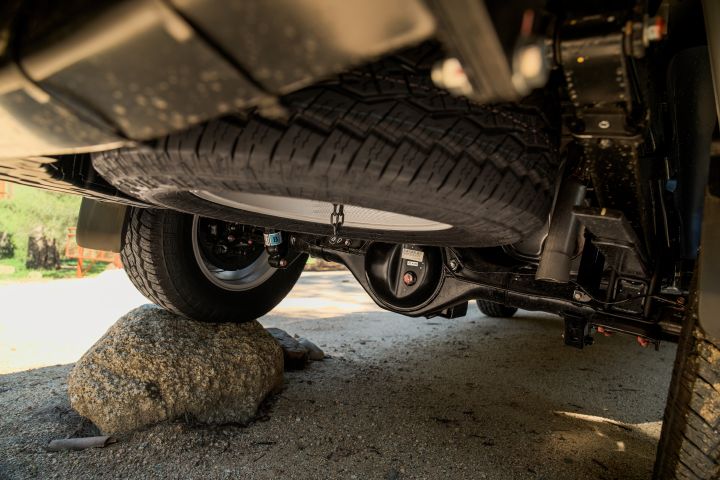 2026 Nissan Navara ST dual cab ute finished in Summit Silver captured underneath, focusing on the spare tyre, axle housing and rock obstacle beneath the chassis.