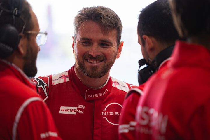 Oliver Rowland spricht lächelnd mit dem Team, während er seinen roten Rennanzug des Nissan Formula E Teams trägt.