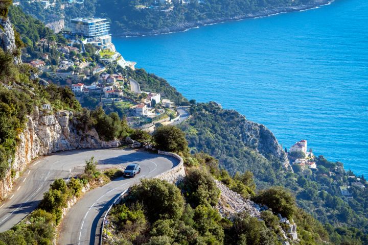Prise de vue dynamique d'un Ariya NISMO après un virage en épingle avec vue sur la mer en arrière-plan.