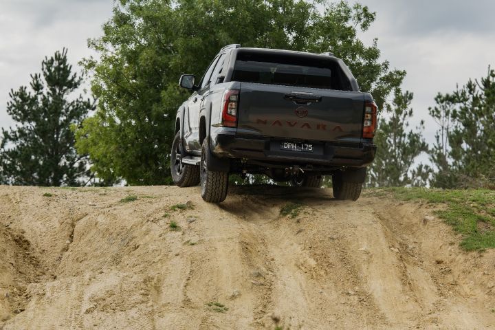 2026 Nissan Navara PRO-4X finished in Boulder Grey viewed from the rear cresting a ridge, showing tailgate badgework, high‑mounted stop light and visible exhaust tip.