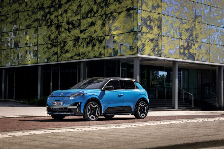 Blick von schräg vorne auf einen blauen Nissan Micra, der vor einer Glasfassade mit grünen Malereien stehen