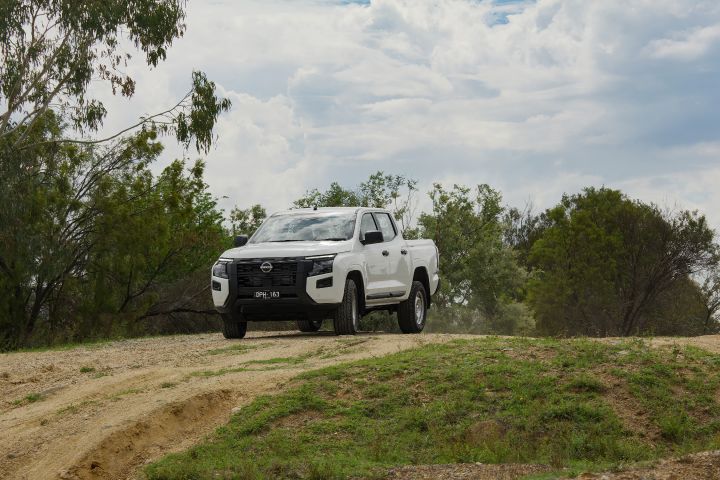 2026 Nissan Navara SL dual cab ute finished in Alpine White captured from a distance on a ridge-top dirt path, with rutted terrain and bushland surroundings.