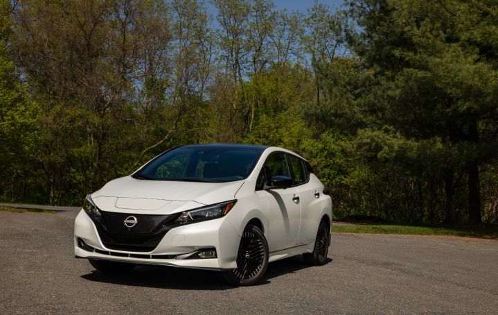 Front left 3/4 view of a white 2025 Nissan LEAF parked in front of a wooded area.
