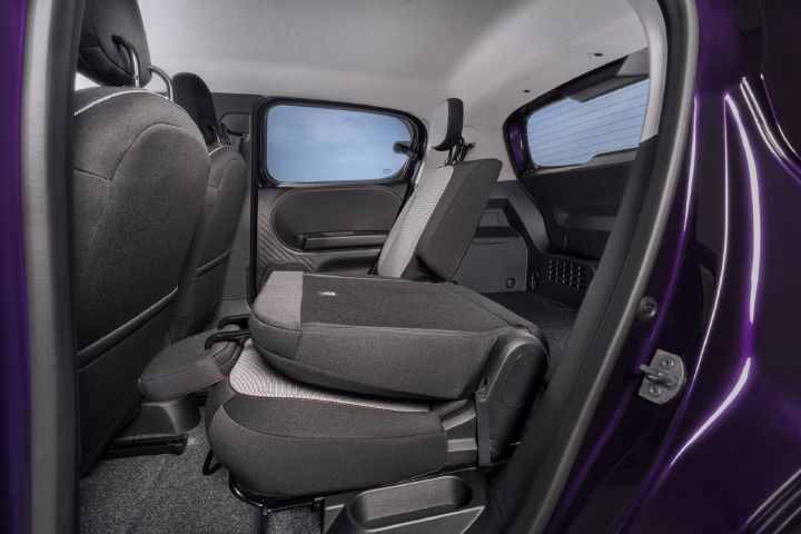 Das Foto zeigt den hinteren Fahrgastraum eines Kleinwagens mit grauer Polsterung, violettem Türrahmen, getönten Scheiben und schwarzem Teppichboden. Der hintere Sitz auf der linken Seite ist nach vorne geklappt, wodurch die flexible Sitzanordnung und das vergrößerte Kofferraumvolumen deutlich werden.