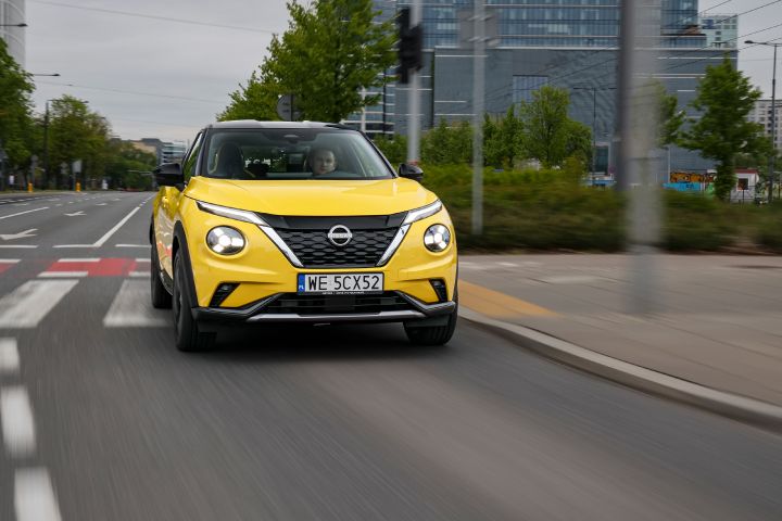 Jadący żółty Nissan Juke (widok z przodu) z budynkami w tle