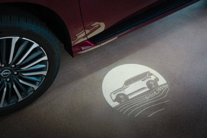 A floor illumination in the shape of an Armada with text below is seen next to a red 2025 Nissan Armada.