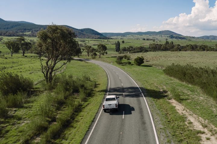 2026 Nissan Navara SL dual cab ute finished in Alpine White seen from above on a winding rural road through green fields and rolling hills.