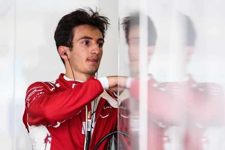Gabriele Minì bereitet sich in seinem roten Rennanzug des Nissan Formula E Teams und mit seinen Ohrhörern auf eine Trainingseinheit vor. Sein Spiegelbild ist auf der weißen Garagenwand zu sehen.