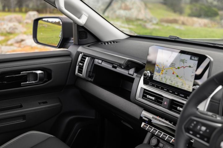 Passenger-side dashboard view inside a 2026 Nissan Navara ST-X, showing the open upper storage compartment above the glovebox, dashboard trim, and the 9-inch Touch infotainment screen displaying a navigation map.