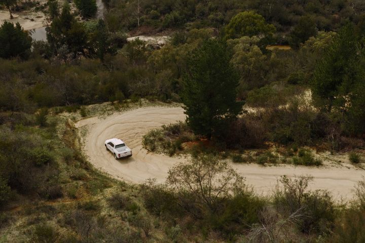 2026 Nissan Navara SL dual cab ute finished in Alpine White viewed from a high aerial angle rounding a wide sandy bend through bushland.