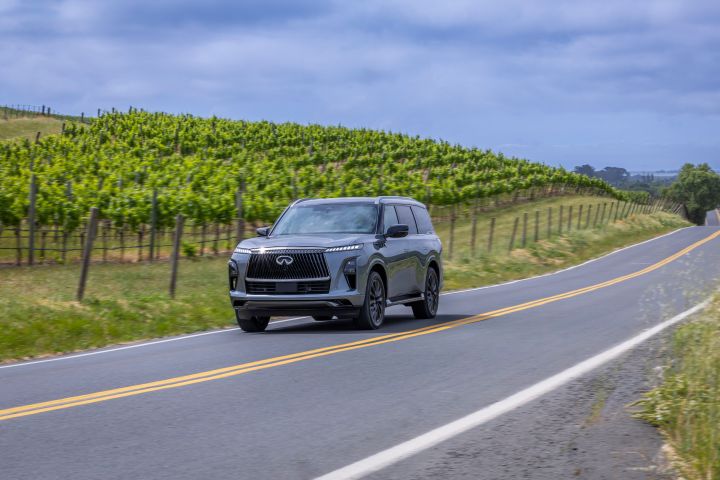 ブドウ畑を背景に田舎道を走るダークグレーのINFINITI QX80 SUV