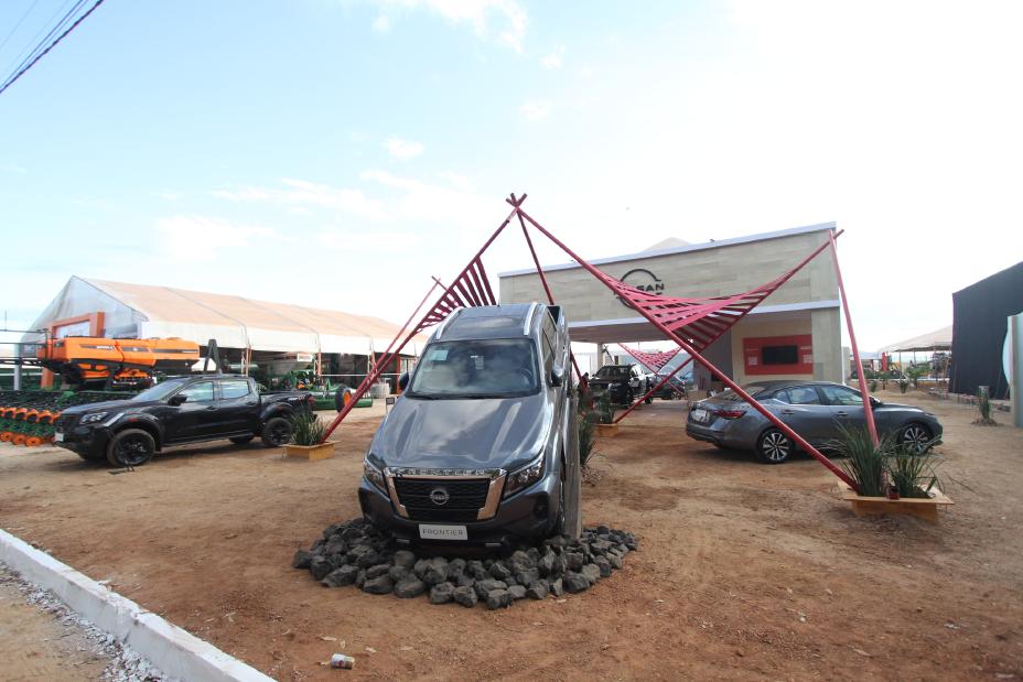 Picape Nissan Frontier suspendida e em destaque no stande da Nissan na Agrotins ao redor de outros carros